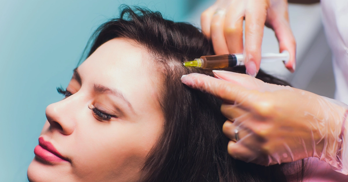 Woman receiving PRP for Hair in Mesa, AZ, syringe near scalp, eyes closed, blue background.